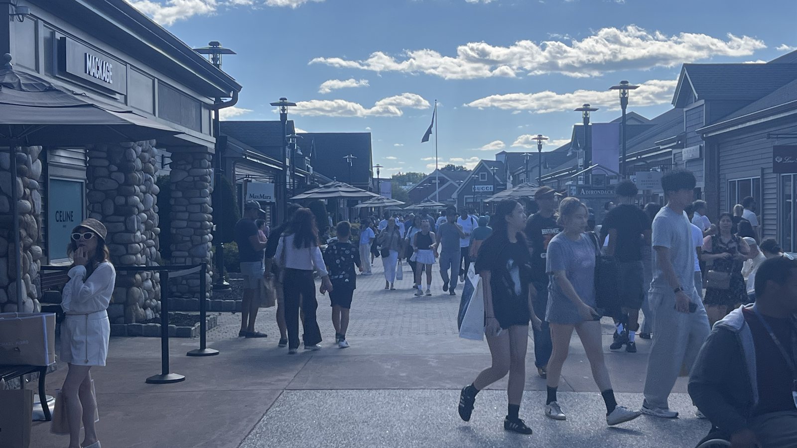 Woodbury Common's pedestrian street in the late afternoon, shoppers heading away past the Mackage, Celine and Max Mara storefronts