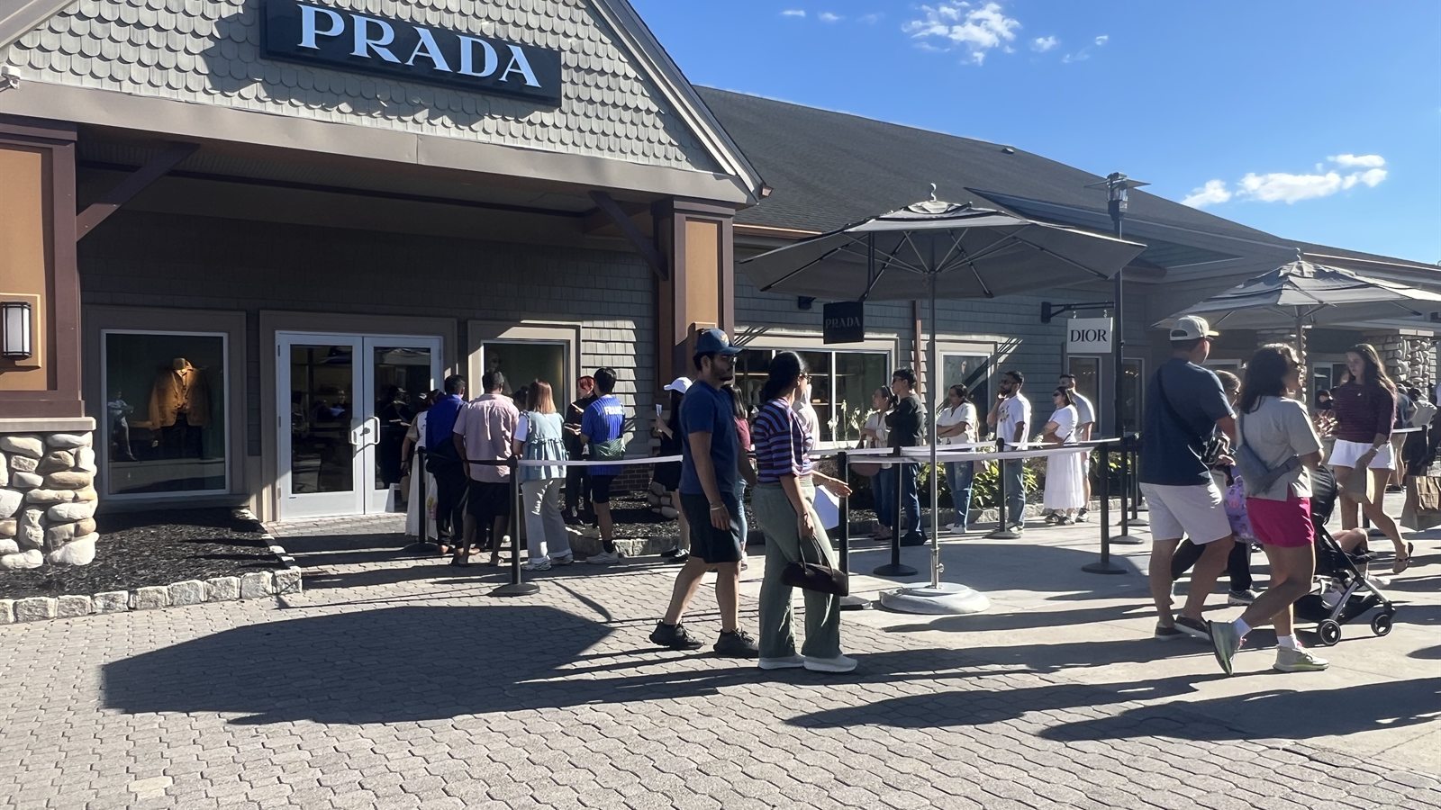 Queue outside Prada at Woodbury Common, with the Dior sign next door