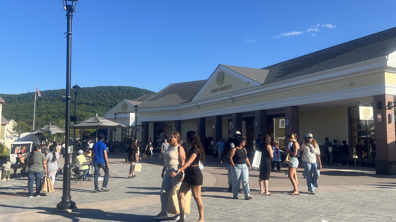 Shoppers carrying bags across the plaza in front of the Tory Burch store at Woodbury Common